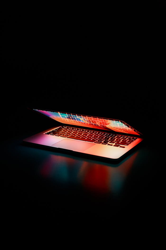 why-choose-us Laptop partially opened, emitting vibrant multicolored lights in dark setting.
