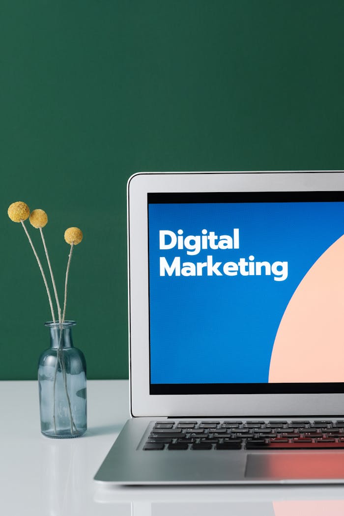 journey A laptop displaying 'Digital Marketing' with a minimalist floral decor in a glass vase.